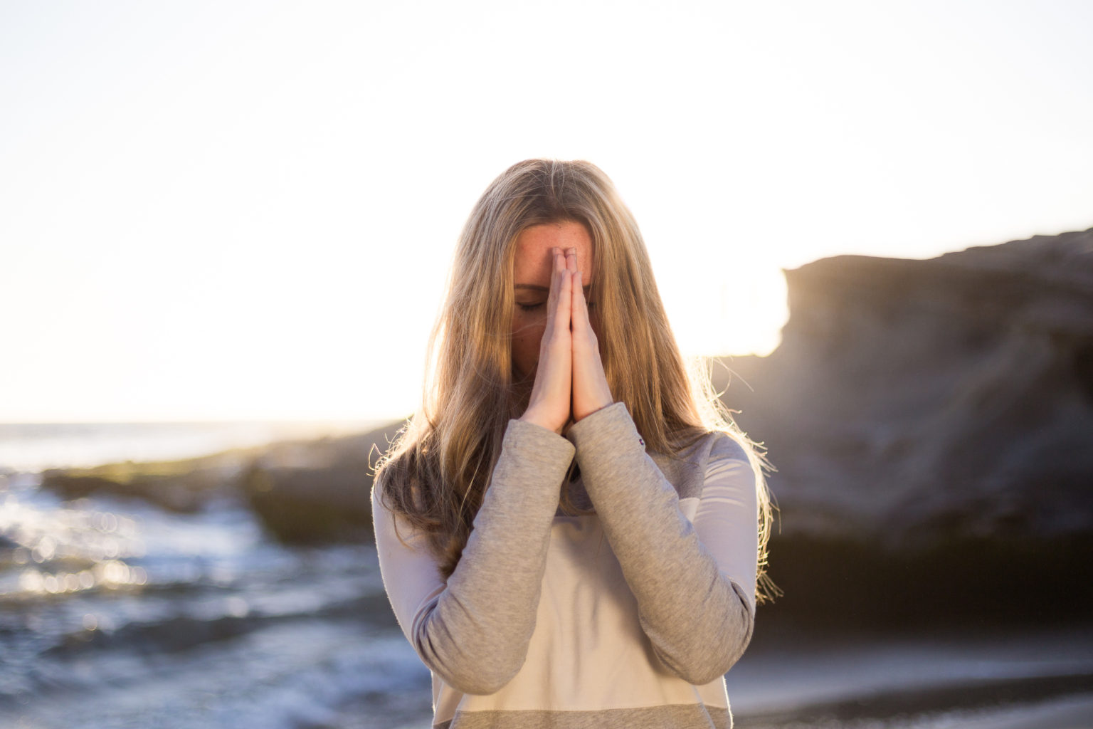 Woman with hands in prayer mode at the beach representing caregivers